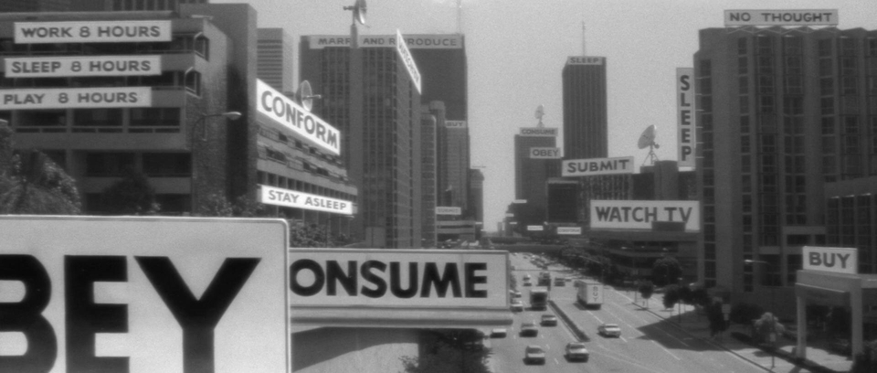 A still frame from the film They Live shows the world in black and white, with all advertising billboards replaced with subliminal messages: "CONSUME", "OBEY", "WATCH TV", "BUY".